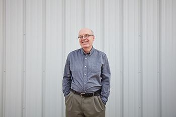 A smiling bald man  is wearing glasses and a blue shirt